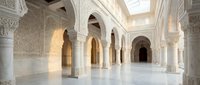 Elegant Islamic architecture interior with ornate white marble columns, intricate geometric patterns, and arched doorways creating serene mosque or palace space.