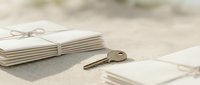 Vintage brass key placed on sandy surface next to tied envelopes and blank papers, suggesting secrets, correspondence, or unlocking memories for design projects.