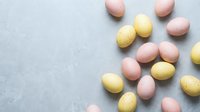 Pastel pink and yellow speckled Easter eggs scattered on a gray stone background with copy space for spring holiday designs.