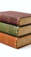 Stack of three antique books with worn leather spines in burgundy, green, and orange tones, featuring aged pages and wooden covers. Suitable for education, literature, library, and vintage design projects.