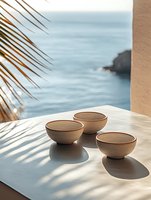 Ceramic bowls on marble table with ocean view and palm leaf shadow, creating serene coastal atmosphere for luxury resort dining.