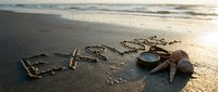 Word explore written in wet sand on a sunny beach with a compass and seashells, evoking adventure and travel inspiration.