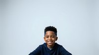 Young African American boy with short dark hair smiling at camera wearing navy blue shirt against white background for portrait and commercial use.