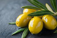 Fresh green olives with leaves on dark stone background, macro food photography showing texture and natural shine of Mediterranean appetizer.