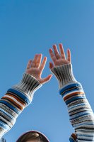 Raised hands in striped knit sleeves against bright blue sky, expressing freedom, joy and achievement. Low angle view captures uplifting moment.