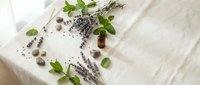 Natural lavender essential oil bottle with fresh herbs and dried flowers on white wooden background for aromatherapy and wellness spa treatments.