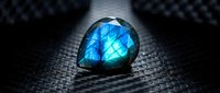 Stunning blue labradorite gemstone with brilliant flash on dark textured surface showcasing natural iridescent colors and mineral beauty for jewelry design.