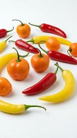 Colorful hot chili peppers variety including red, yellow and orange peppers scattered on white background for cooking and spice ingredients.