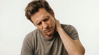Middle-aged Caucasian man experiencing neck pain and discomfort, holding his neck with concerned expression, health and wellness concept for medical content.