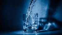 Fresh water pouring into glass with ice cubes against blue background, suitable for beverage, hydration, wellness and refreshment advertising campaigns.