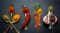 Colorful spices and herbs arranged on wooden spoons over dark slate background. Culinary ingredients for cooking and seasoning food preparation.