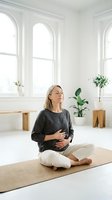 Pregnant woman meditating in bright modern room with arched windows. Expectant mother practicing mindfulness yoga on mat in minimalist white interior.