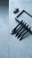 Modern black kitchen utensils and natural stones arranged on concrete surface for minimalist cooking and food preparation styling.