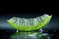 Fresh green lime slice with water drops and splash on dark background with reflection, macro photography for fresh beverage and cocktail advertising.