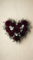 Heart-shaped arrangement of burgundy dahlia flowers with eucalyptus leaves on neutral textured background for romantic occasions and floral design projects.