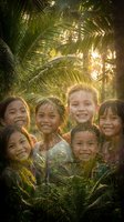 Happy diverse children group smiling together under tropical palm trees with warm golden sunlight filtering through leaves creating joyful summer vacation atmosphere.