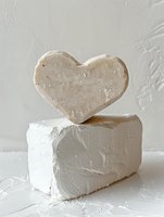 Heart-shaped stone balanced on a white plaster block against a textured wall, minimal love concept in neutral tones for decor or Valentine designs.