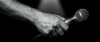 Close-up of male hand gripping microphone in dramatic black and white lighting for music performance, broadcasting, and entertainment industry concepts.
