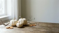 White pumpkins and autumn leaves on rustic wooden table near window. Minimalist fall decor for seasonal home styling and harvest celebrations.