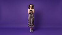 Young woman with curly hair using smartphone on purple background. Casual female texting, browsing social media in studio setting for digital lifestyle concepts.
