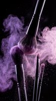 Professional makeup brushes with purple powder explosion on black background for cosmetic and beauty industry advertising.