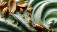 Creamy pistachio dessert with whole nuts scattered on textured green surface, showcasing rich texture and natural ingredients for food photography.