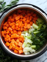 Fresh diced carrots, chopped celery stalks and parsley leaves in stainless steel pressure cooker pot, ready for cooking healthy homemade soup or stew.