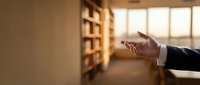 Man in business suit reaching toward bookshelf in library, symbolizing knowledge acquisition, education, and professional development in workplace learning environment.