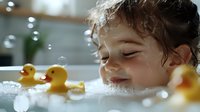 Happy toddler boy with curly hair enjoying bath time with yellow rubber ducks, splashing water droplets creating joyful childhood moment for parenting content.