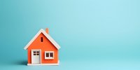 Small orange house model with white trim on turquoise background for real estate mortgage insurance property investment home ownership concept.