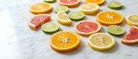 Fresh citrus fruit slices including orange, grapefruit, lemon and lime arranged on white marble surface for healthy eating and vitamin C nutrition.