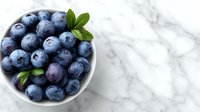 Fresh blueberries in white bowl with mint leaves on marble background. Healthy organic superfood for breakfast, smoothies and desserts.