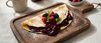 Delicious crepe filled with chocolate spread and fresh berries on rustic wooden board, gourmet breakfast dessert with powdered sugar dusting.