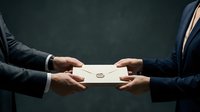 Two businessmen in dark suits exchanging sealed envelope with wax stamp in professional corporate setting against dark background for business deals.