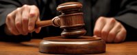 Judge striking wooden gavel in courtroom during legal proceedings, close up view of hands and ceremonial hammer on brown desk, dramatic lighting.