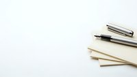 Silver fountain pen with cap on stack of cream colored paper sheets against clean white background for office and writing projects.