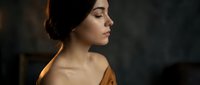 Young woman with elegant updo hairstyle in warm golden lighting against dark background, perfect for beauty and fashion campaigns, spa treatments, skincare ads.