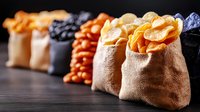 Assorted colorful potato chips in rustic burlap bags arranged in row on dark wooden background, selective focus on crispy snacks with natural lighting.