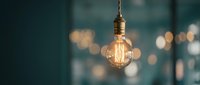 Vintage Edison bulb hanging with warm glowing filament against blurred bokeh background creating cozy atmospheric lighting for interior design.