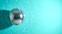 Shiny disco ball reflecting light rays on turquoise background creating sparkle effect for party and nightclub entertainment events.