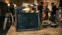 Vintage film production clapper board on wooden surface with cinema equipment and blurred crew members in background, used for movie production and filmmaking projects.