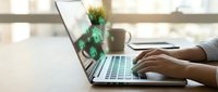 Hands typing on laptop with glowing green house icons floating from screen, symbolizing online real estate search and property investment concept.