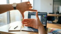 Professional designer hands framing composition at modern workspace with laptop and color swatches for creative project planning and visual development.