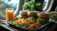Fresh salmon and bagel sandwiches on serving tray with orange juice, vegetables and microgreens in morning light, breakfast composition with healthy food.