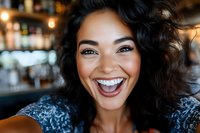Young African American woman with curly hair and bright smile laughing joyfully at camera in cozy bar setting. Natural genuine emotions and happiness concept.