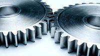 Industrial metal gears with precision teeth meshing together on white background. Mechanical engineering components for manufacturing automation systems.