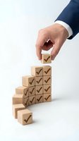 Businessman hand placing wooden block with checkmark on staircase pyramid structure, symbolizing business growth, success, and achievement goals for corporate strategy.