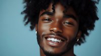 Happy young African American man with curly hair smiling broadly against blue background. Positive emotions, joy, confidence and cheerful expression.