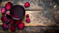 Fresh beetroot juice in glass with sliced raw beets on rustic wooden background. Healthy detox drink rich in vitamins and antioxidants for wellness lifestyle.