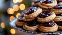 Homemade butter cookies with dark chocolate ganache and raspberry jam filling on vintage plate, festive bokeh lights background, holiday dessert.